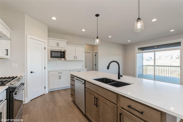 kitchen featuring light stone countertops, stainless steel appliances, sink, white cabinetry, and hanging light fixtures