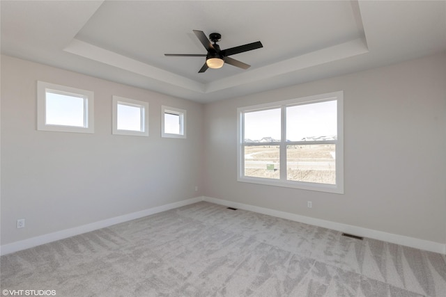 carpeted spare room with a tray ceiling and ceiling fan