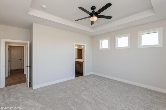 unfurnished bedroom with ensuite bath, ceiling fan, light carpet, and a tray ceiling