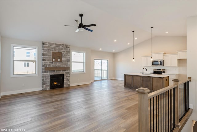 kitchen featuring a center island with sink, stainless steel appliances, ceiling fan, a fireplace, and light hardwood / wood-style flooring