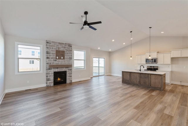 unfurnished living room featuring lofted ceiling, light wood-type flooring, a fireplace, ceiling fan, and sink