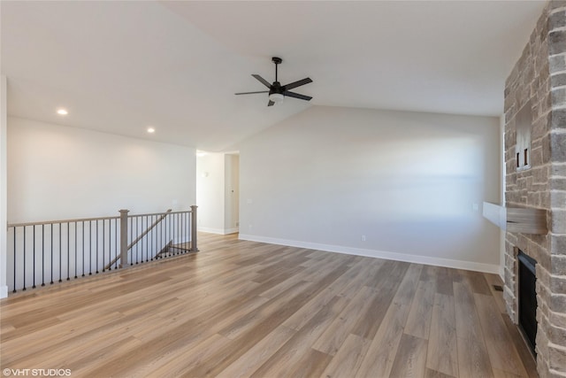 unfurnished living room featuring ceiling fan, light hardwood / wood-style flooring, a stone fireplace, and lofted ceiling