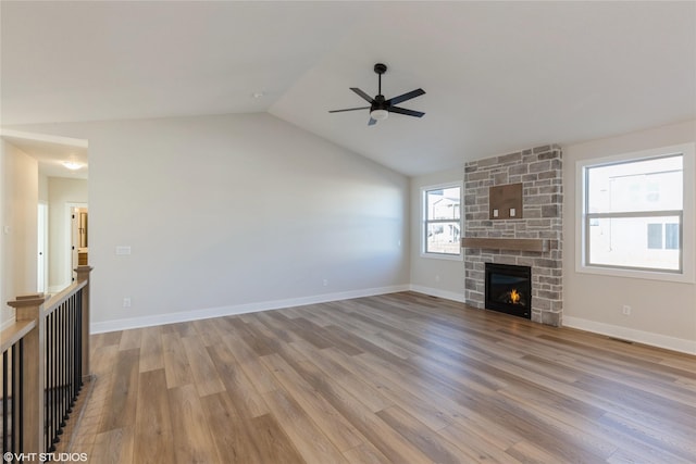 unfurnished living room with lofted ceiling, light wood-type flooring, ceiling fan, and a stone fireplace