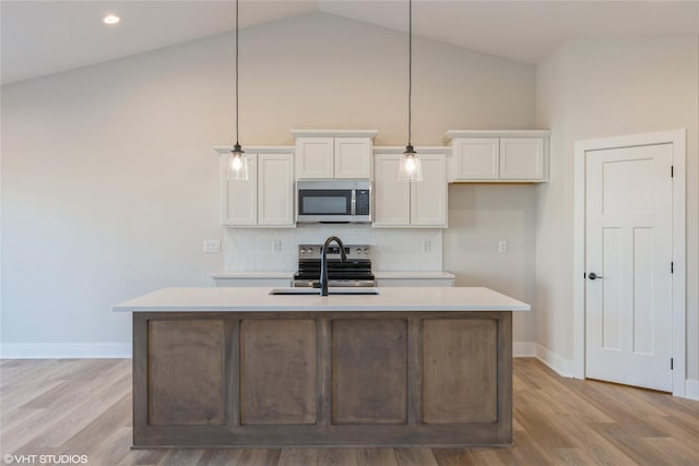 kitchen with appliances with stainless steel finishes, white cabinetry, decorative light fixtures, and a kitchen island with sink