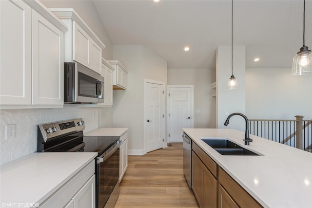 kitchen featuring pendant lighting, stainless steel appliances, light hardwood / wood-style floors, white cabinetry, and sink