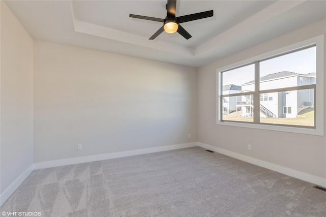 carpeted empty room with ceiling fan and a raised ceiling