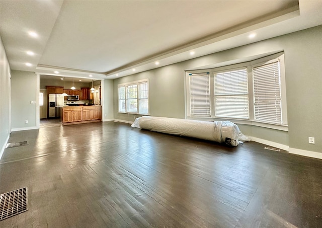 unfurnished bedroom featuring stainless steel refrigerator with ice dispenser, a tray ceiling, and dark wood-type flooring