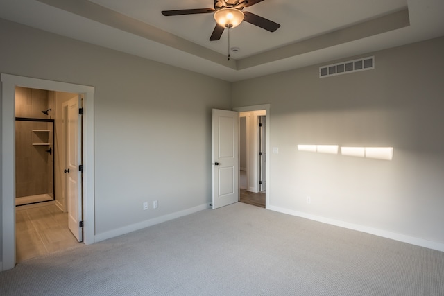 unfurnished bedroom with a tray ceiling, a walk in closet, ceiling fan, and light colored carpet