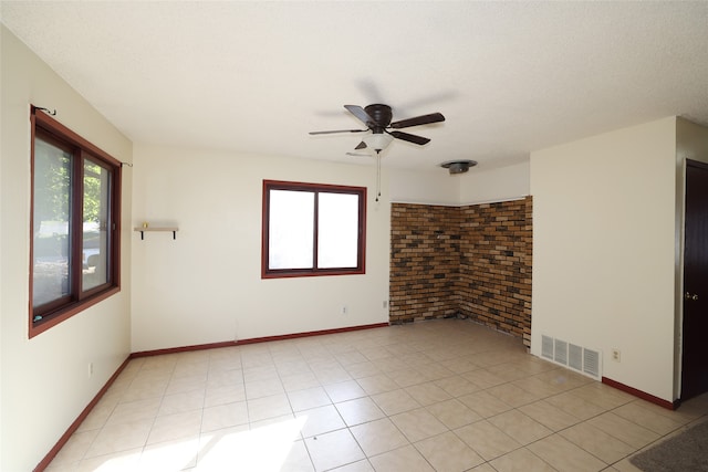 unfurnished room with ceiling fan, a textured ceiling, brick wall, and a wealth of natural light