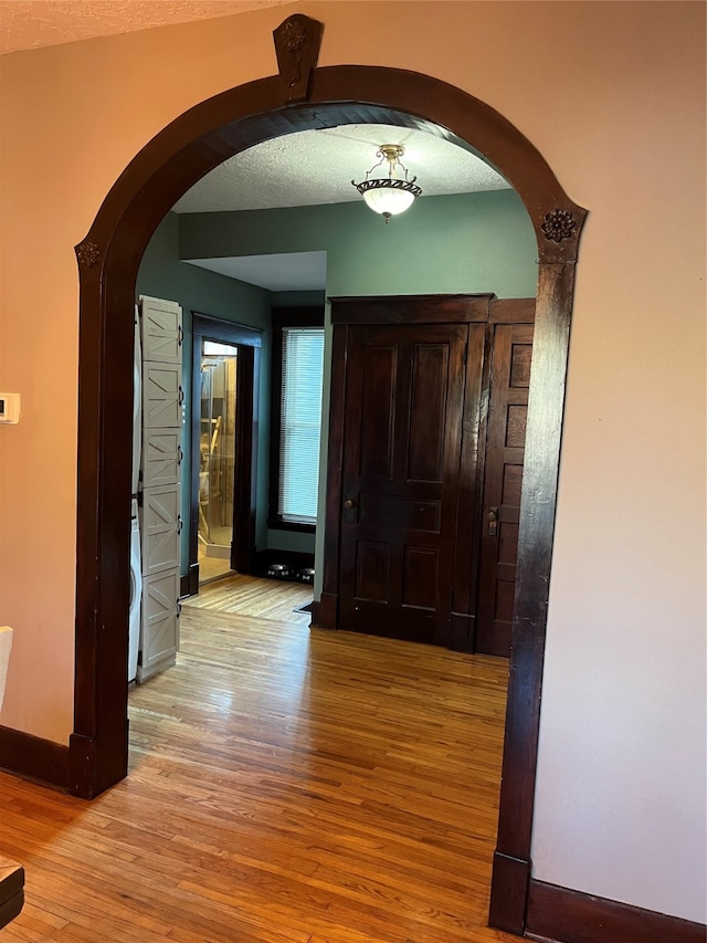 hall with a textured ceiling and light hardwood / wood-style flooring