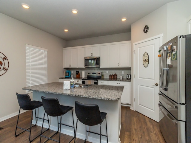 kitchen featuring dark stone countertops, white cabinets, stainless steel appliances, a kitchen island with sink, and dark hardwood / wood-style floors