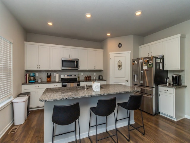 kitchen with decorative backsplash, white cabinetry, stainless steel appliances, a center island with sink, and dark hardwood / wood-style floors