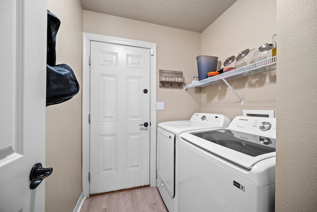 washroom featuring a textured ceiling, light hardwood / wood-style floors, and washing machine and clothes dryer