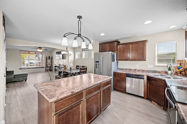 kitchen with sink, a kitchen island, decorative light fixtures, stainless steel appliances, and light hardwood / wood-style floors