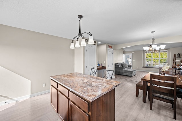 kitchen featuring light wood-type flooring, hanging light fixtures, a center island, an inviting chandelier, and light stone countertops