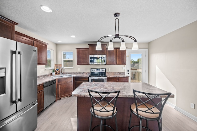 kitchen featuring decorative light fixtures, appliances with stainless steel finishes, a wealth of natural light, and a kitchen island