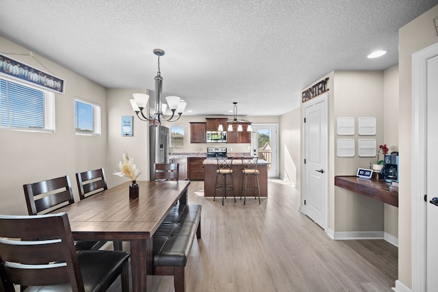 dining space featuring a textured ceiling, light hardwood / wood-style flooring, sink, and a notable chandelier