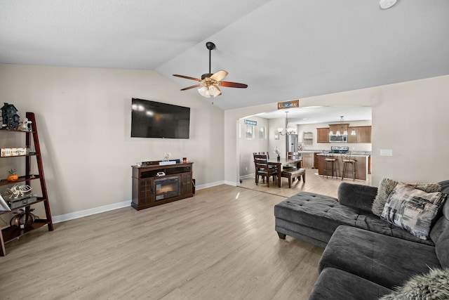 living room featuring ceiling fan with notable chandelier, light hardwood / wood-style floors, and vaulted ceiling