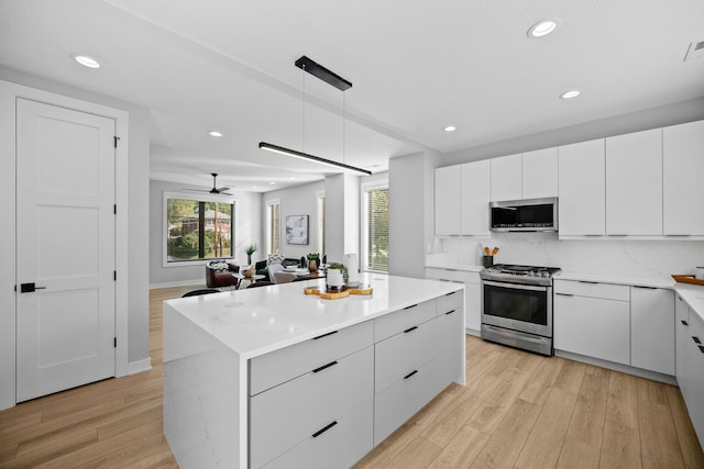 kitchen with pendant lighting, stainless steel appliances, light countertops, open floor plan, and white cabinetry