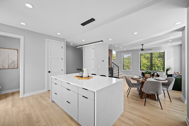 kitchen featuring light wood finished floors, a center island, decorative light fixtures, light countertops, and white cabinetry