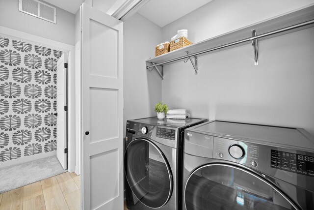 washroom with light wood finished floors, laundry area, separate washer and dryer, and visible vents