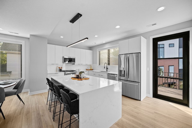 kitchen with white cabinets, a kitchen island, decorative light fixtures, stainless steel appliances, and a wealth of natural light