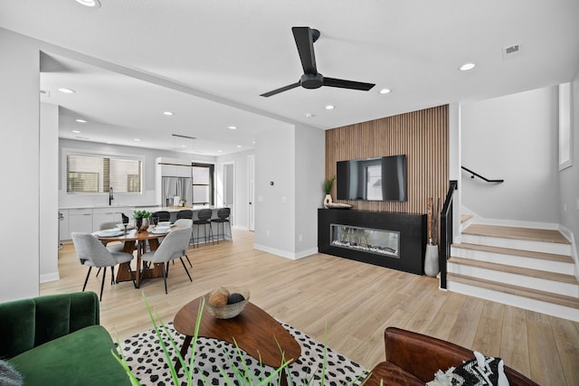 living area featuring light wood-type flooring, stairs, baseboards, and a glass covered fireplace