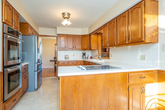 kitchen with decorative backsplash, kitchen peninsula, sink, and appliances with stainless steel finishes