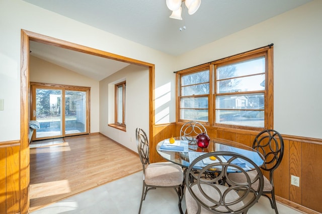 dining area with wooden walls, ceiling fan, lofted ceiling, and light wood-type flooring