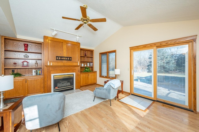 living room featuring a textured ceiling, ceiling fan, light hardwood / wood-style flooring, and lofted ceiling