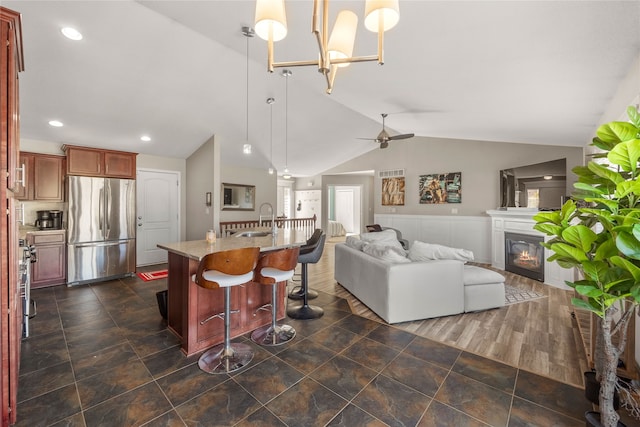 kitchen with hanging light fixtures, sink, stainless steel refrigerator, a breakfast bar area, and vaulted ceiling