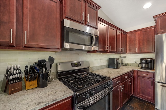 kitchen with dark tile patterned floors, lofted ceiling, decorative backsplash, stainless steel appliances, and light stone countertops