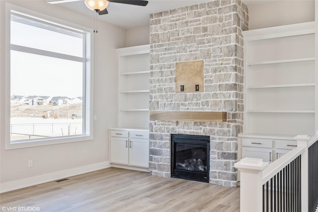 unfurnished living room with ceiling fan, light hardwood / wood-style flooring, and a stone fireplace