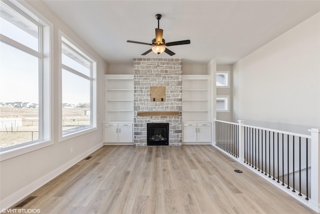 unfurnished living room with ceiling fan, a wealth of natural light, light hardwood / wood-style flooring, and a stone fireplace