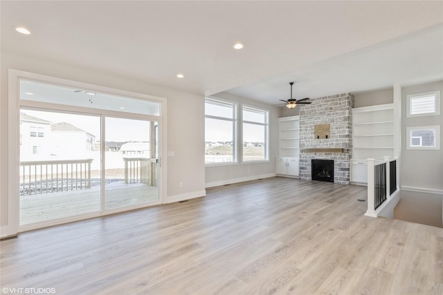 unfurnished living room with light wood-type flooring, ceiling fan, a stone fireplace, and built in shelves