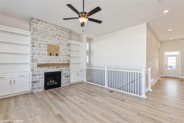 unfurnished living room featuring ceiling fan, light hardwood / wood-style floors, and a stone fireplace