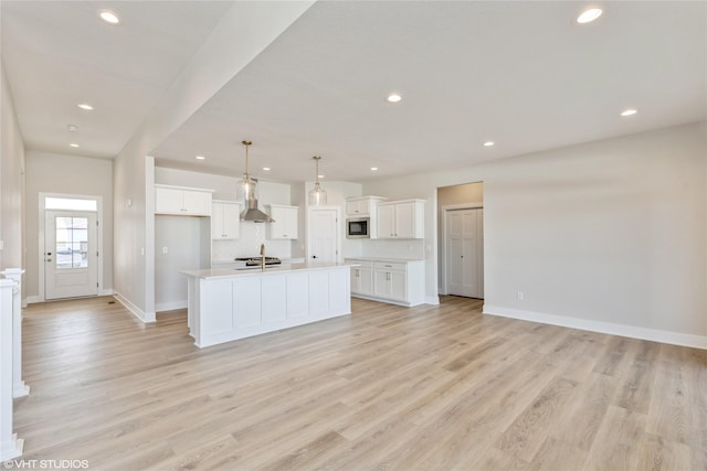 kitchen with decorative light fixtures, white cabinets, a kitchen island with sink, and built in microwave