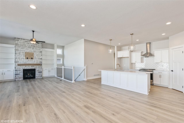 kitchen with an island with sink, wall chimney range hood, stainless steel stove, white cabinets, and sink