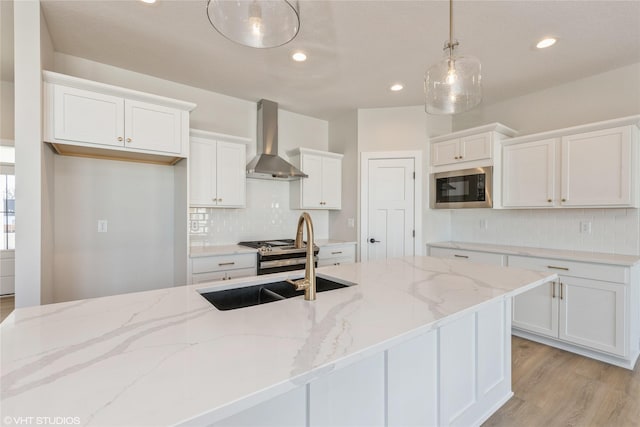 kitchen featuring built in microwave, hanging light fixtures, wall chimney range hood, white cabinets, and sink