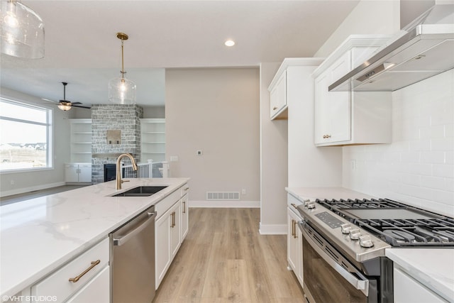 kitchen with decorative light fixtures, sink, white cabinetry, appliances with stainless steel finishes, and wall chimney exhaust hood