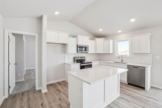 kitchen with a center island, stainless steel appliances, lofted ceiling, white cabinets, and sink