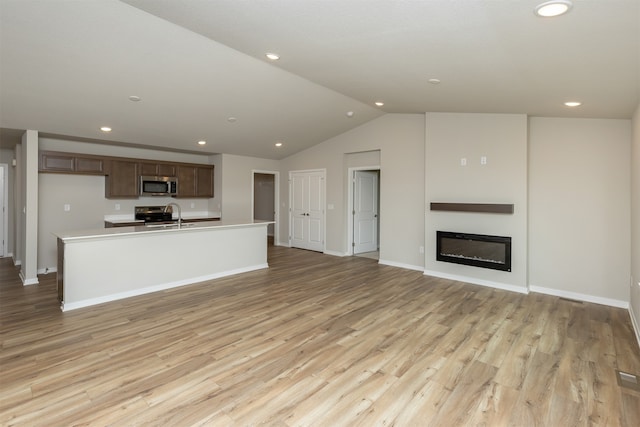 unfurnished living room featuring sink, light hardwood / wood-style flooring, and lofted ceiling