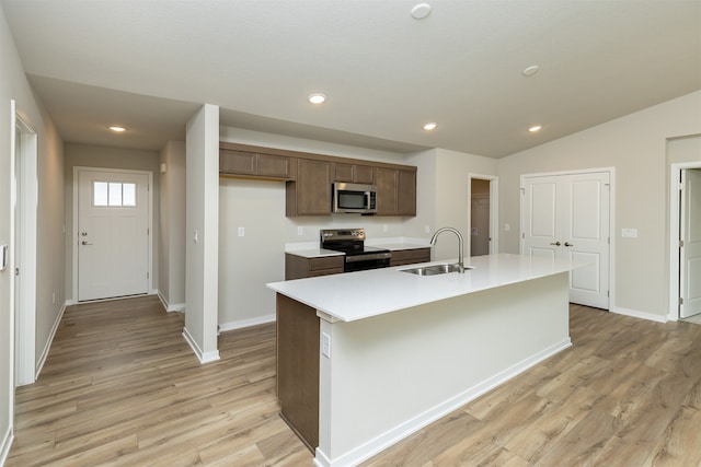 kitchen with an island with sink, sink, light wood-type flooring, and appliances with stainless steel finishes