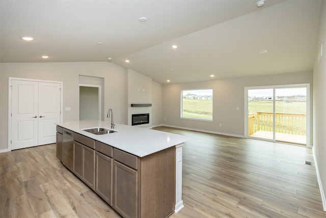 kitchen with light wood-type flooring, sink, vaulted ceiling, and a center island with sink