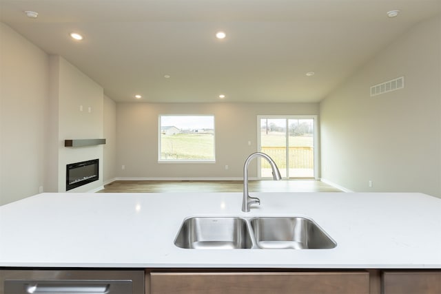 kitchen featuring sink, light stone countertops, an island with sink, light wood-type flooring, and vaulted ceiling