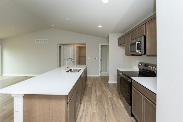 kitchen with a center island with sink, stainless steel appliances, sink, vaulted ceiling, and light hardwood / wood-style floors