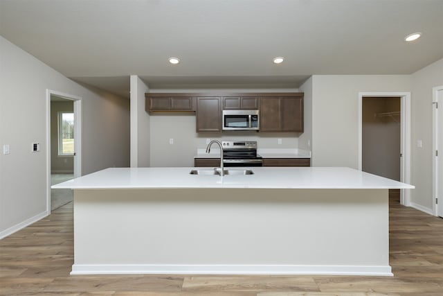 kitchen featuring a center island with sink, dark brown cabinetry, sink, light wood-type flooring, and appliances with stainless steel finishes