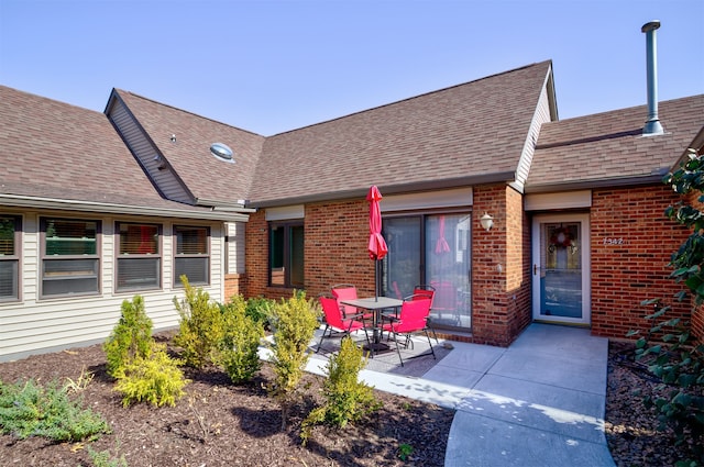 doorway to property featuring brick siding, a patio area, and a shingled roof