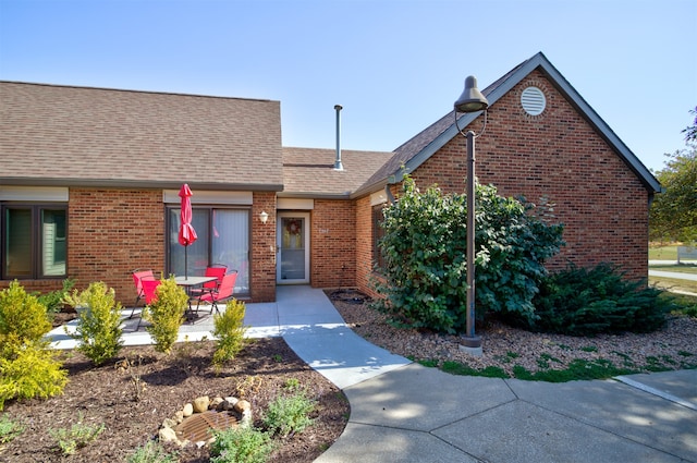 view of front of property with a patio area, brick siding, and a shingled roof