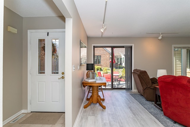 foyer entrance with a healthy amount of sunlight, rail lighting, light hardwood / wood-style floors, and a textured ceiling